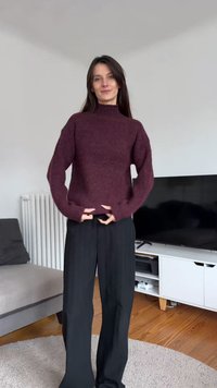 Bordó kötött pulóver magas nyakkal és széles ujjakkal, fekete, texturált anyagú, széles szárú nadrággal kombinálva.