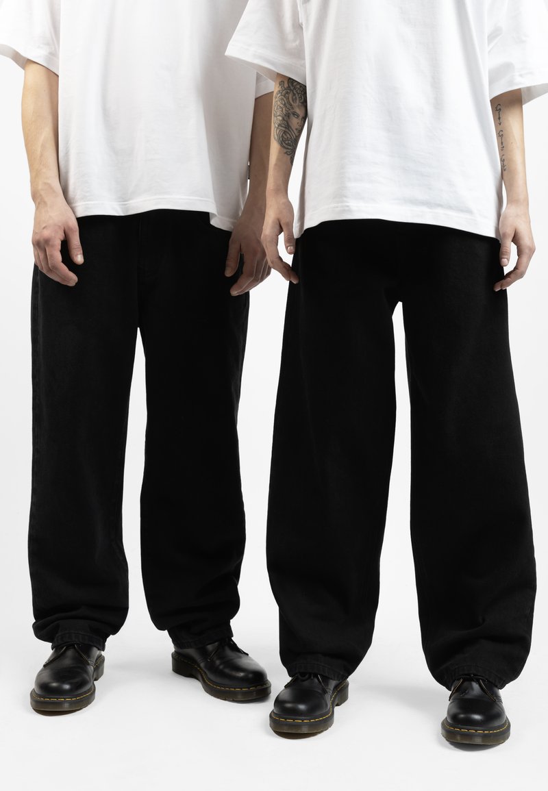 Pantaloni neri larghi con polsini elasticizzati, abbinati a t-shirt bianche oversize e scarpe nere con lacci e suola gialla.