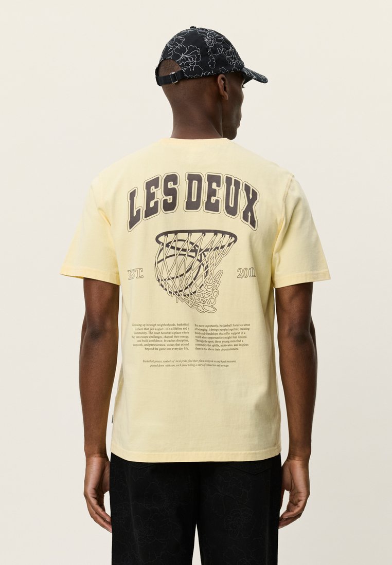 Κίτρινη κοντομάνικη μπλούζα με γραφικό ενός μπασκετικού διχτυού και κείμενο στην πλάτη. Κατασκευασμένη από βαμβάκι με άνετη εφαρμογή.