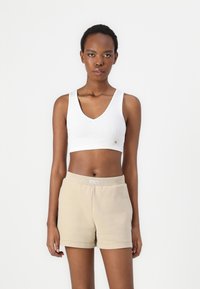 Bjeli rebrasti crop top s V-izrezom i malim logom na prsima, u kombinaciji s bež kratkim hlačama s elastičnim pojasom i preklopom.