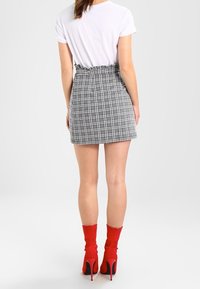 Jupe mini à carreaux gris avec une taille haute, associée à un haut blanc à manches courtes et des escarpins rouges de style chaussette. Tissu lisse, design ajusté.