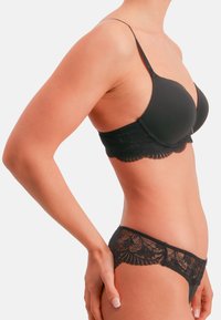 Schwarzer Spitzen-BH mit glatten Cups und verstellbaren Trägern, ergänzt durch passende Spitzen-Slips mit gezacktem Rand. Elegantes Design.