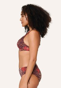 Top de bikini con estampado de leopardo y tirantes ajustables, acompañado de una parte inferior alta a juego en tonos cálidos de rojo y marrón, con acentos florales.