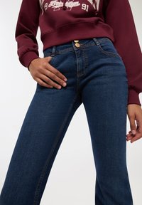 Ciemnoniebieskie dżinsy o wysokim stanie, z złotymi guzikami, minimalnym przeszyciem i lekko zwężanym krojem nogawek.