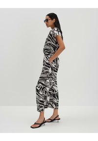 Combinaison à imprimé zèbre noir et blanc à manches courtes, taille élastique, poches latérales, coupe ample, associée à des sandales noires à talons.