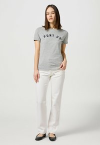 Camiseta de algodón gris con el texto "PONY UP" en color azul marino, combinada con pantalones blancos. Presenta un corte clásico y mangas cortas, exhibida en un modelo.