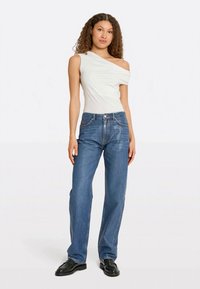 White off-shoulder top paired with blue denim jeans. The jeans are straight-leg with a classic five-pocket design and subtle stitching.