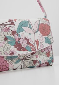 Floral crossbody bag in white faux leather features pink, red, and green flower patterns, a flap closure, and a thin shoulder strap.