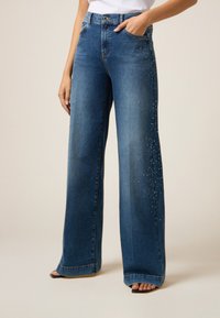 Lage blauwe denim jeans met wijde pijpen, een hoge taille, subtiele glinsteraccenten en twee voorzakken, die het casual ontwerp versterken.