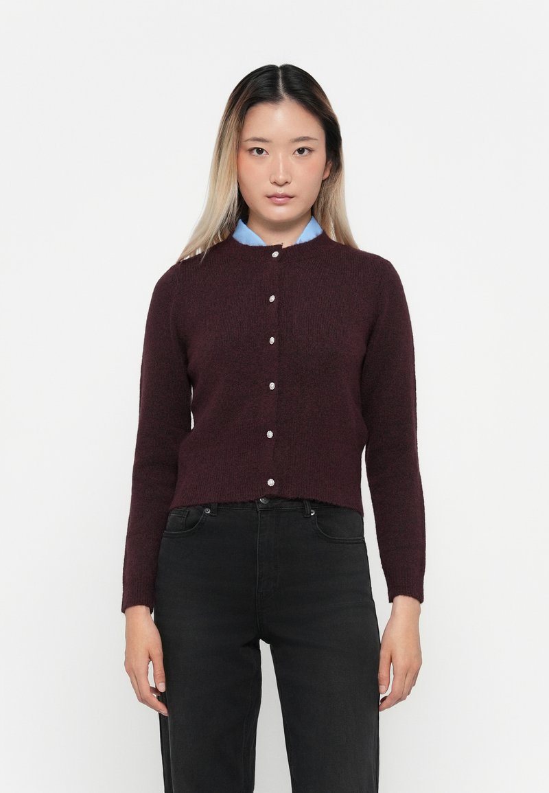 Cardigan bordeaux en maille douce, avec un col rond, des manches longues et des boutons argentés sur le devant.