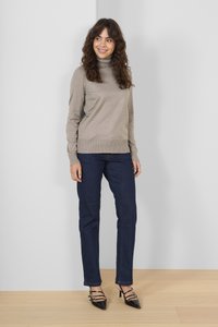 Beiger Turtleneck-Pullover mit geripptem Saum, kombiniert mit dunkelblauen, geraden Jeans und schwarzen, spitz zulaufenden High Heels mit Riemchen-Details.