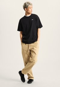 Černé tričko s krátkým rukávem, volné světle béžové kalhoty a černé nazouváky. Jednoduchý design, ležérní styl, minimální akcenty.