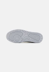 Suela de sneaker blanca de goma con patrones de agarre texturizados y detalles de logotipo, que presenta un emblema ovalado de marca y un diseño de banda de rodadura distintivo.