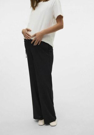 Zwarte wijde broek met een elastische tailleband en koord, gecombineerd met een losse witte t-shirt. Gladde stofstructuur.