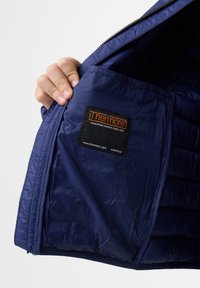 Interno di una giacca isolante blu navy che mostra una texture trapuntata, con un'etichetta nera incorporata che presenta "Thermore" in arancione.