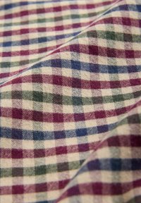 Close-up of wrinkled cotton fabric with a checkered pattern in cream, burgundy, navy blue, and olive green squares.