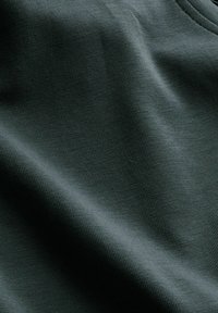 Dark green textured fabric with visible fine ribbed knit pattern and soft folds creating gentle shadows and highlights.