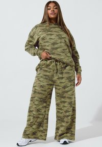 Felpa con stampa camouflage e pantaloni a gamba larga in tonalità di verde. Tessuto morbido e texturizzato con vita regolabile e vestibilità comoda. Sneakers bianche.
