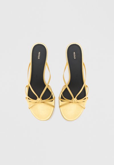 Sandale galbene cu bretele încrucișate, talpă plată și vârf rotunjit. Branț negru cu logo, textură netedă, design minimalist.