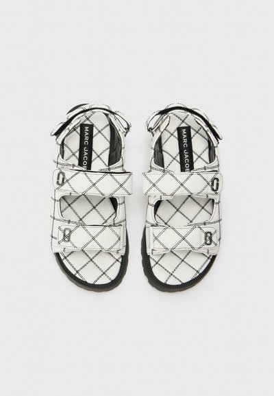 Bílé sandály s prošívaným designem a černým prošíváním. Mají nastavitelné popruhy a texturovanou černou podrážku. Uvnitř je štítek "MARC JACOBS".