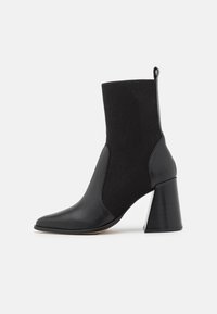 Botines negros con parte superior de tela acanalada y detalles de cuero suave, punta afilada y tacón grueso con una base de color contrastante.