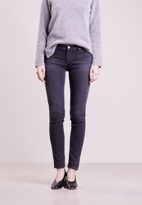 Czarne skinny jeans z metalowym guzikiem i zapięciem na zamek; połączone z szarym swetrem z dzianiny i czarnymi butami na wysokim obcasie.