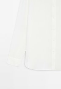 Camicia bianca con bottoni, maniche lunghe, realizzata in tessuto morbido. Presenta un colletto classico e polsini arrotondati con dettagli a bottoni.