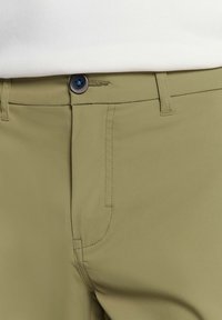 Olijfgroene broek van gladde stof, met een slim fit, voorzien van een knoopsluiting aan de voorkant en zijzakken. Zichtbare stikseldetails.