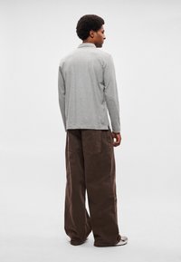 Γκρι μακρυμάνικη μπλούζα συνδυασμένη με υπερμεγέθη καφέ παντελόνια με μεγάλες πίσω τσέπες. Το ύφασμα φαίνεται λείο και με σπορ σχεδιασμό.