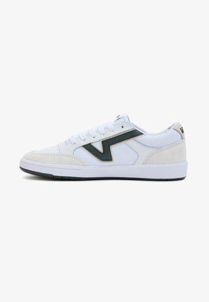 Zapatilla blanca de perfil bajo con franja en zigzag negra, cordones blancos, cuello acolchado, detalles en ante beige y suela blanca con exterior negro.