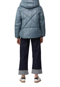 Veste matelassée à capuche de couleur bleu clair mat, avec un motif matelassé. Associée à un pantalon en denim foncé, coupé, et des baskets blanches avec des accents noirs.
