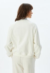 Sudadera de color crema claro con cuello de canalé, hombros caídos y un corte relajado. La tela parece suave con una textura lisa, sin patrones visibles.
