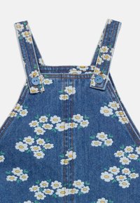 Robe en denim avec imprimé floral de marguerites blanches et jaunes, dotée de bretelles bleues à boutons et de détails de surpiqûres orange.