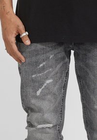 Grå denimjeans med en slitna design och synliga fransar samt lätt nötthet. Slim fit med traditionell femfickorsstil.