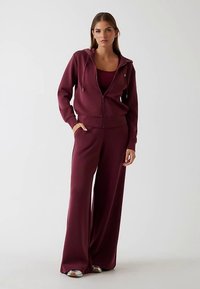 Maroon zip-up hoodie paired with a matching fitted top and wide-leg pants. Soft fabric, relaxed fit, and front pockets in the hoodie.