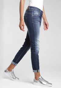 Tmavě modré džíny s úzkým střihem, s manžetami a světle vybledlými. V kombinaci s lesklými stříbrnými teniskami a bílou košilí.