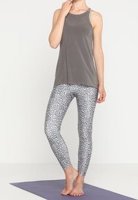 Top gris sin mangas con una textura suave, combinado con leggings de estampado de leopardo blanco y negro. Ambos presentan un diseño ajustado adecuado para ropa de actividad.