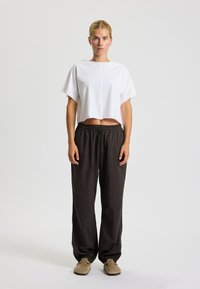 Weißes, kurz geschnittenes T-Shirt mit kurzen Ärmeln, kombiniert mit lockeren schwarzen Hosen mit elastischem Bund und gerafften Bündchen. Hellbraune Slipper.