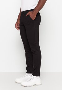 Zwarte broek van een gladde stof, met een slim fit, zijzakken en lussen voor een riem. Gecombineerd met chunky witte sneakers.