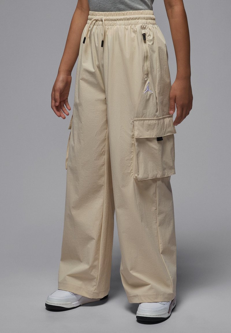 Beige cargo pants with elastic waistband, two side pockets, and one back pocket. Made from lightweight, textured material. Logo accent near waist.