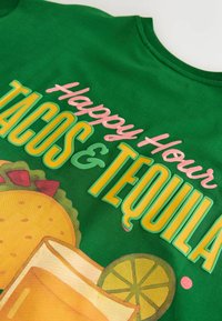 Tissu vert avec texte coloré « Happy Hour Tacos & Tequila » et illustrations d'un taco, d'un shot de tequila et de tranches de citron vert.