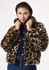 Chaqueta de pelo sintético de estampado de leopardo con una silueta relajada, cuello alto y una superficie suave y texturada. Llevada sobre una camisa de mezclilla.