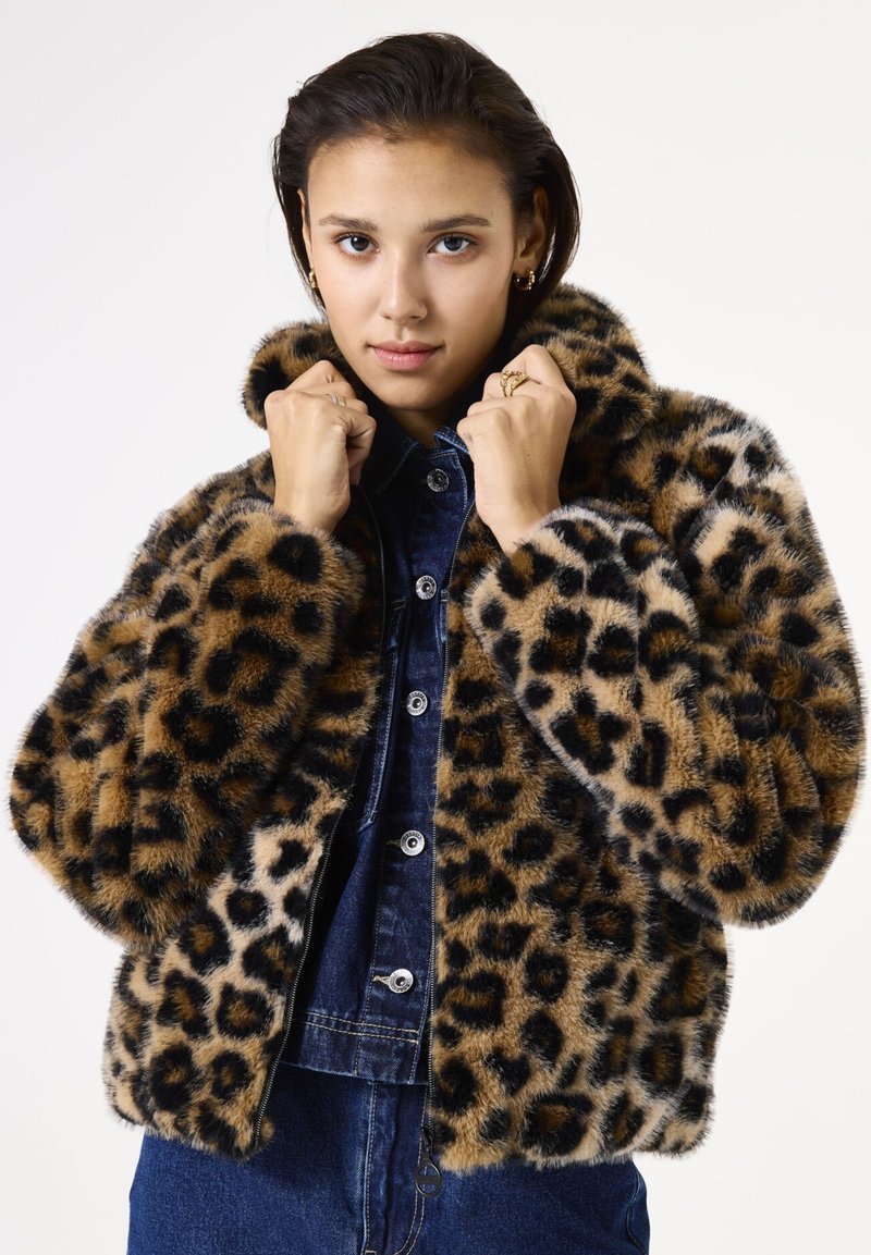 Chaqueta de pelo sintético de estampado de leopardo con una silueta relajada, cuello alto y una superficie suave y texturada. Llevada sobre una camisa de mezclilla.