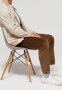 Light beige herringbone jacket, white t-shirt, brown corduroy pants, white sneakers on a gray chair with wooden legs and black hardware.