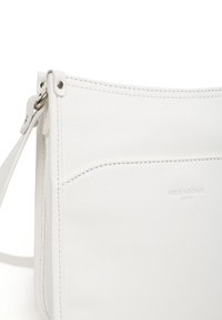 Biała skórzana torba typu crossbody z teksturowaną powierzchnią, minimalistycznym designem, subtelnym haftem i małą przednią kieszonką. Wytłoczone logo.