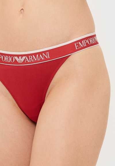 Red thong underwear featuring a branded elastic waistband with "Emporio Armani" in white text and a smooth, soft fabric texture.
