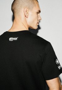 Czarny bawełniany T-shirt z okrągłym dekoltem, logo na plecach i na prawym rękawie. Gładka tekstura oraz dopasowany krój.