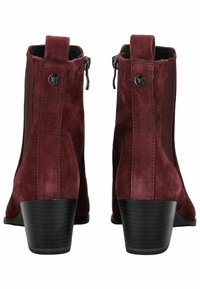 Par de botas de ante burdeos hasta el tobillo con tacones apilados negros, cremalleras laterales y lengüetas, vistas desde atrás sobre un fondo blanco.