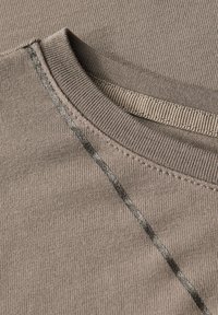 Tissu côtelé marron présentant un col rond, avec un détail de couture grise contrastante le long de la couture de l'épaule et du col.