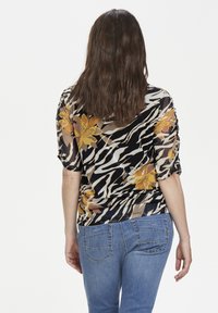 Blusa a stampa floreale nei colori nero, giallo e beige con maniche corte, abbinata a jeans blu chiaro e un tessuto testurizzato.